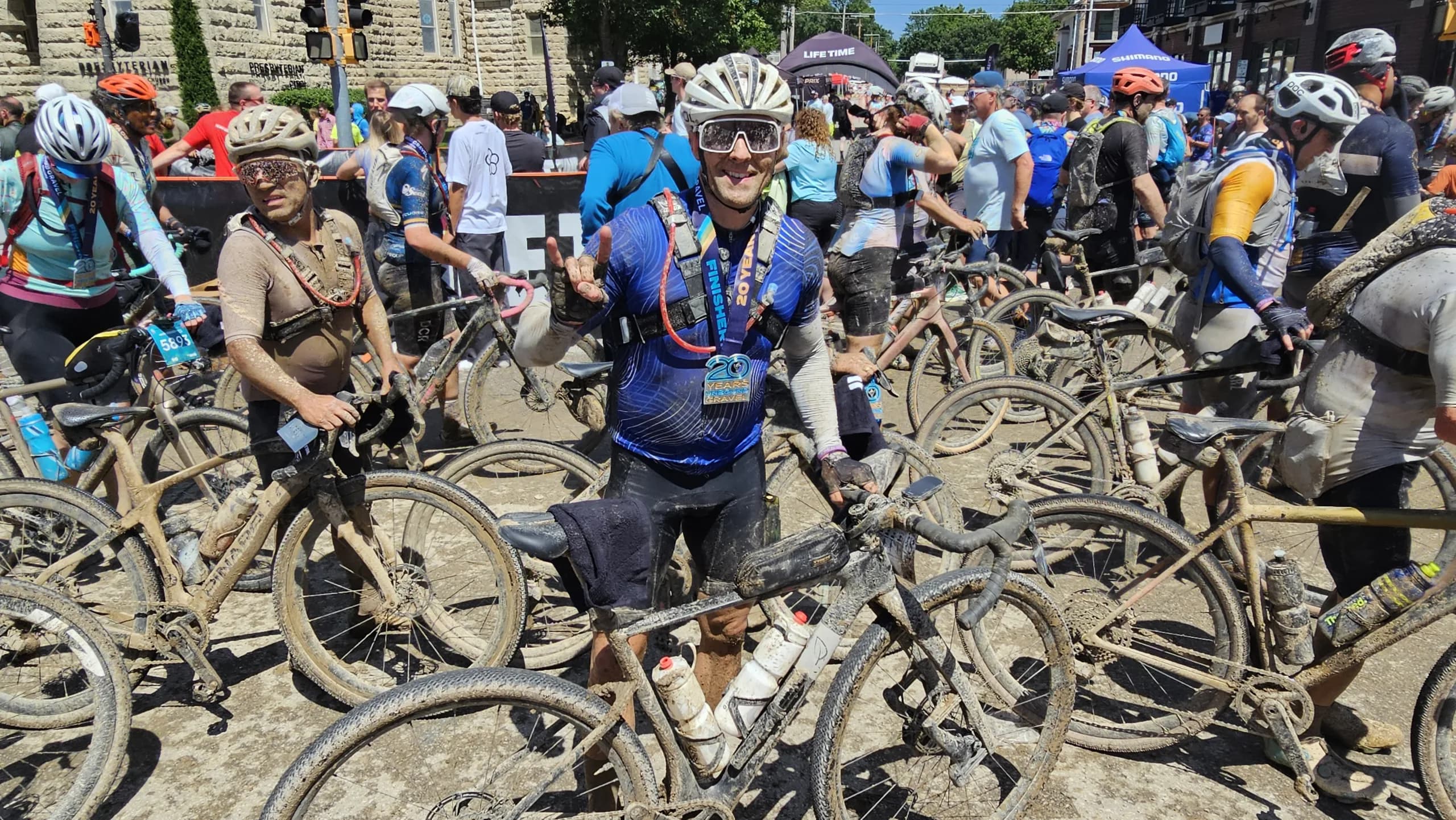 Carey Rouse covered in mud at the Unbound Gravel finish, medal on